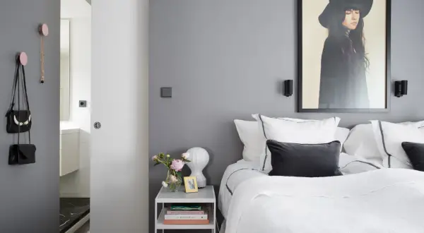 Pareti camera da letto grigia e bianche, con letto bianco, quadro di una donna con cappello e accessori appesi.