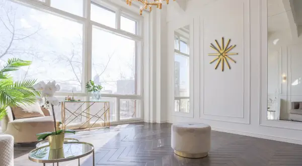 Un elegante soggiorno con un divano beige, tavolini rotondi in vetro e oro, e un orologio da parete dorato. Grigio e oro stanno bene insieme, creando un'atmosfera sofisticata.