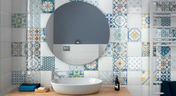 Bagno con lavabo su mobile in legno, specchio rotondo e pareti decorate con vivaci cementine bagno dai motivi geometrici e floreali.