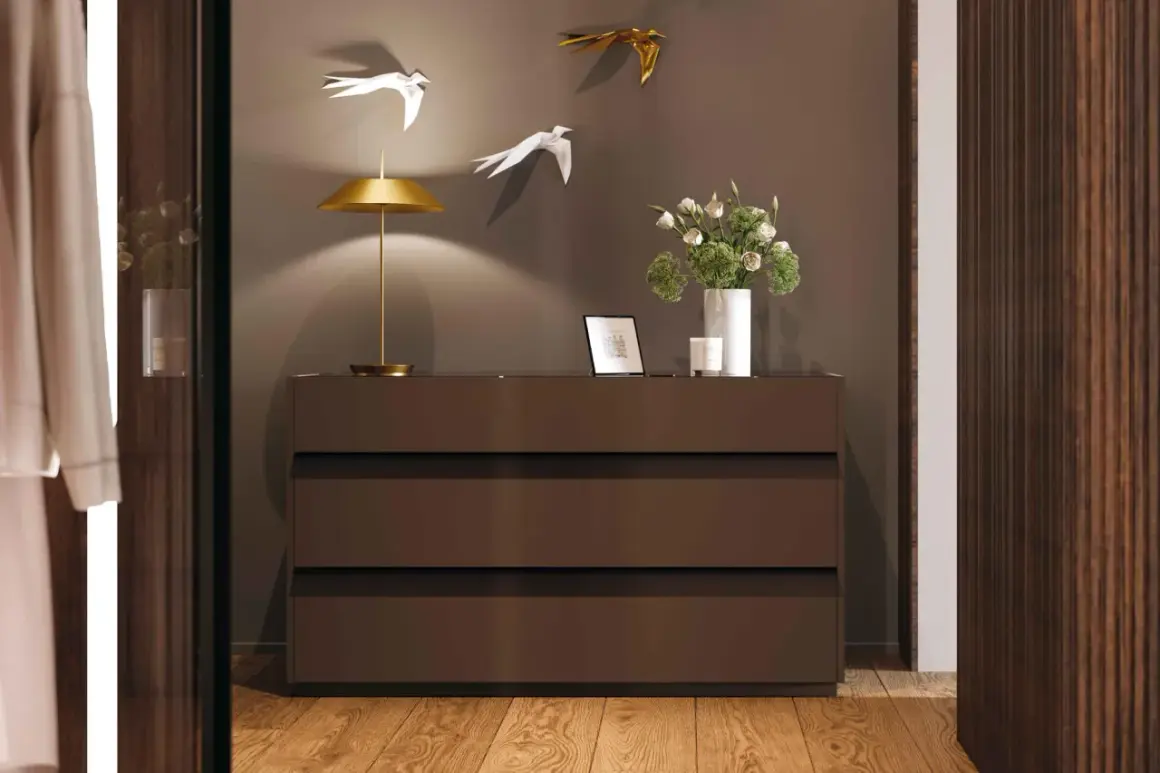 Cosa mettere sul como' della camera da letto moderna: lampada dorata, fiori in vaso bianco, cornice e candela.