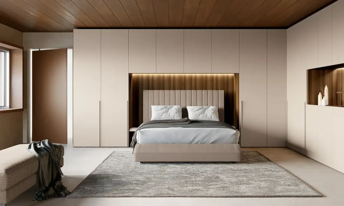 Una moderna zona notte all'ingresso, con letto centrale, armadi a muro e un pouf.