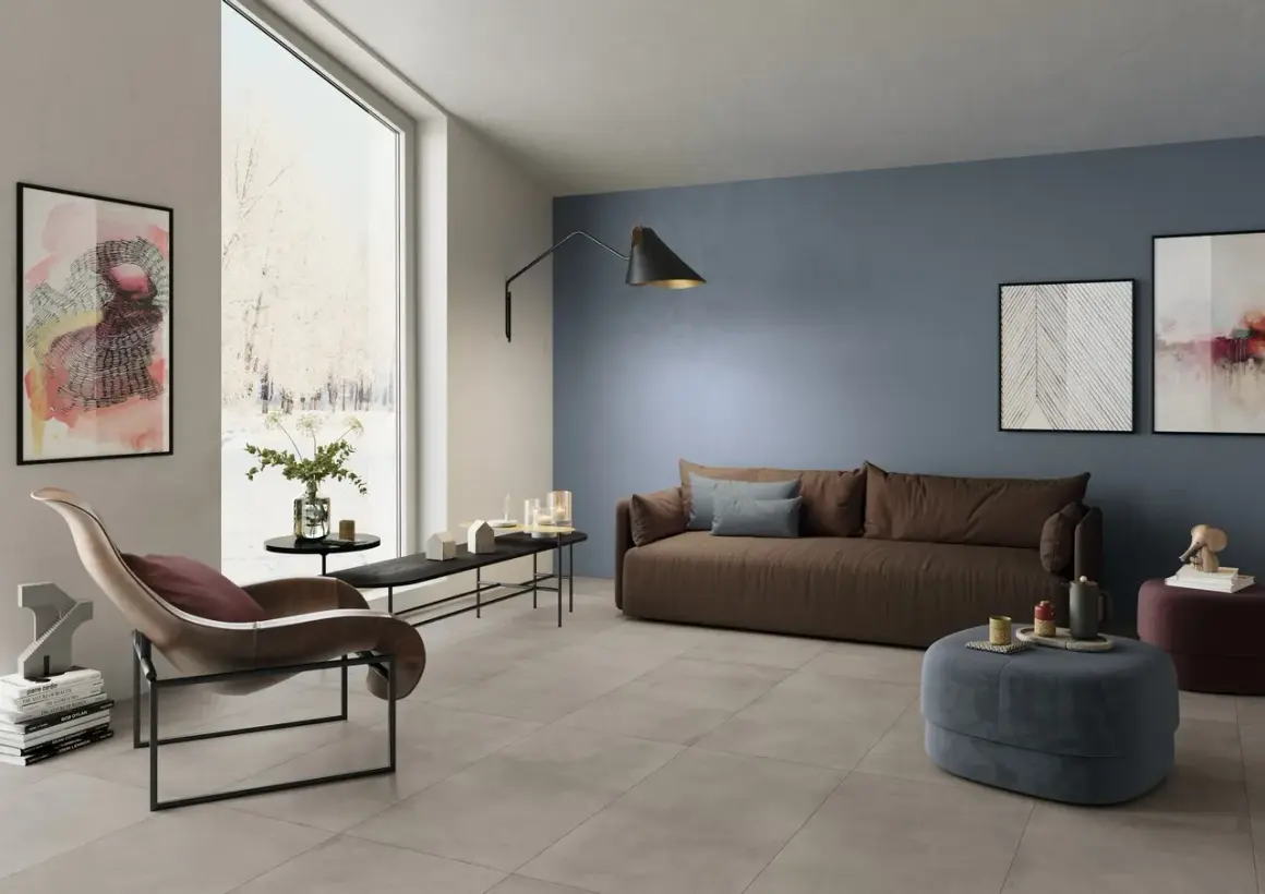 Soggiorno moderno con **pavimento grigio** e **pareti tortora** che creano un'atmosfera rilassante. Divano marrone, poltrona di design e opere d'arte completano l'arredo.