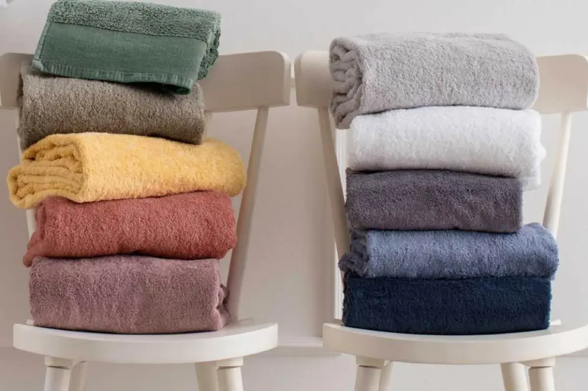 Ecco come piegare gli asciugamani in modo elegante: pile di asciugamani colorati e neutri disposti su sedie bianche.