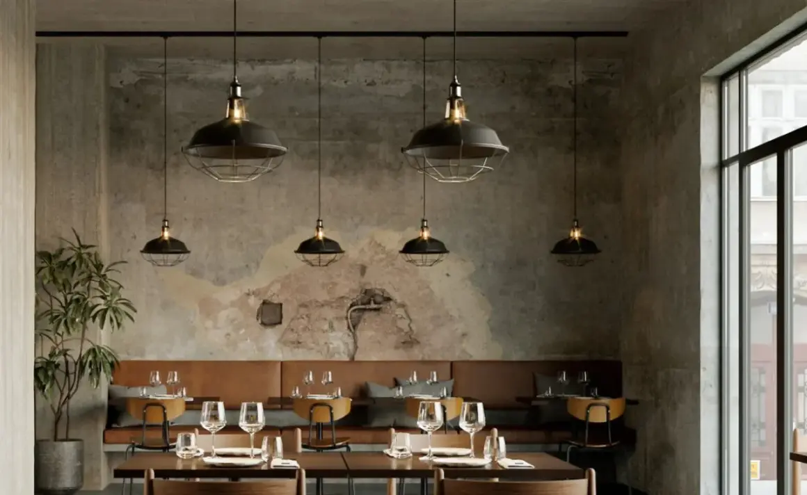 Un elegante lampadario a binario con sei luci industriali illumina un ristorante con pareti in cemento grezzo e divanetti in pelle marrone.