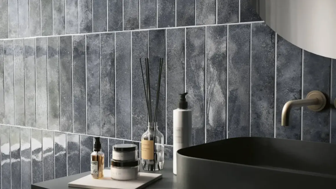 Un elegante bagno azzurro e grigio con piastrelle verticali, lavabo nero e rubinetto dorato.