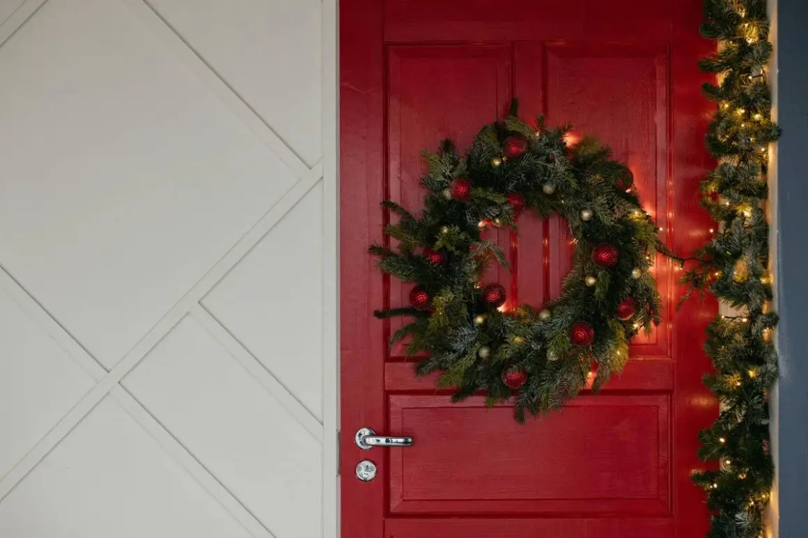 Un ingresso natalizio da sogno: una porta rossa con ghirlanda di pino, palline rosse e luci dorate per abbellire porta ingresso natale.