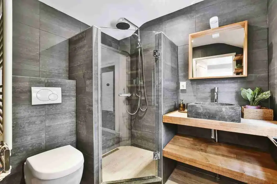 Bagno grigio chiaro e bianco con doccia in vetro, lavabo in pietra e specchio in legno.