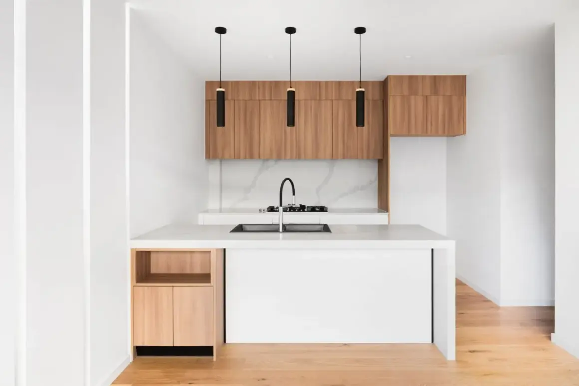Cucine piccole particolari con isola bianca, pensili in legno e tre lampade nere sospese.
