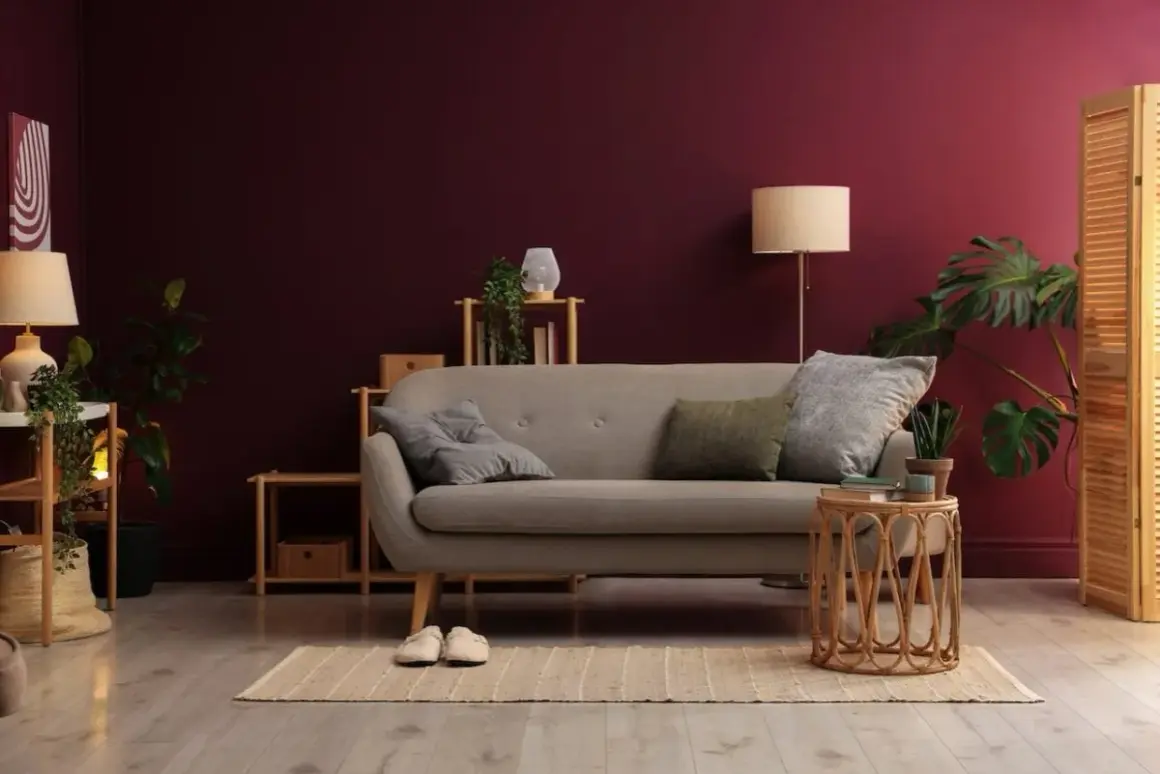 Soggiorno accogliente con divano grigio, piante verdi e pareti color vinaccia intenso.