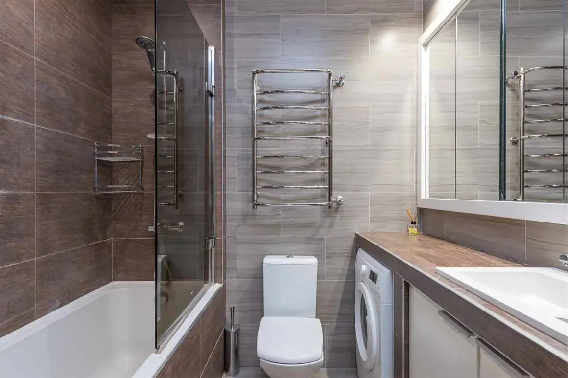 Bagno moderno con vasca, doccia, WC e una pratica lavatrice integrata sotto il lavandino.