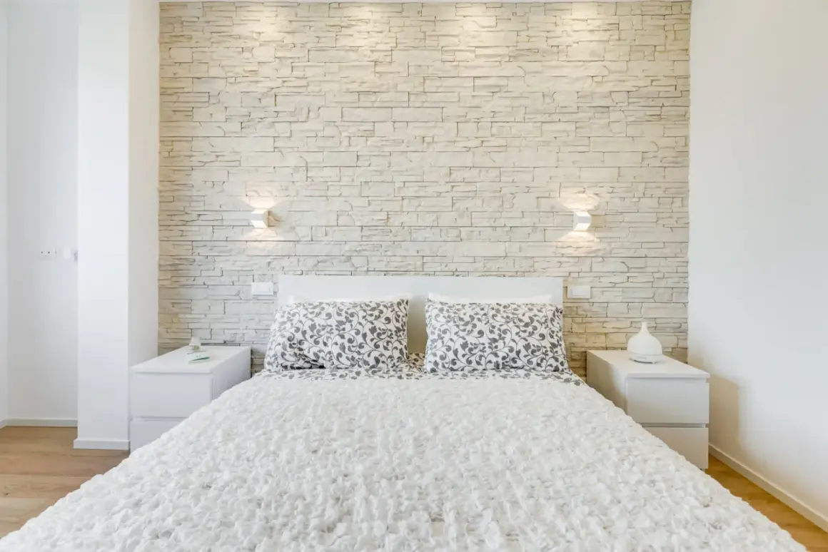 Accogliente camera da letto moderna con una suggestiva parete in pietra che fa da sfondo al letto.