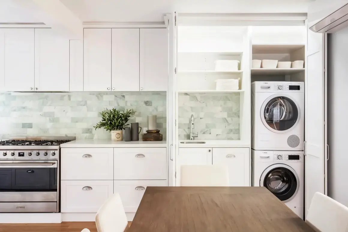 Soluzione elegante per come nascondere lavatrice e asciugatrice in una cucina moderna, integrate in una nicchia con ante a scomparsa.