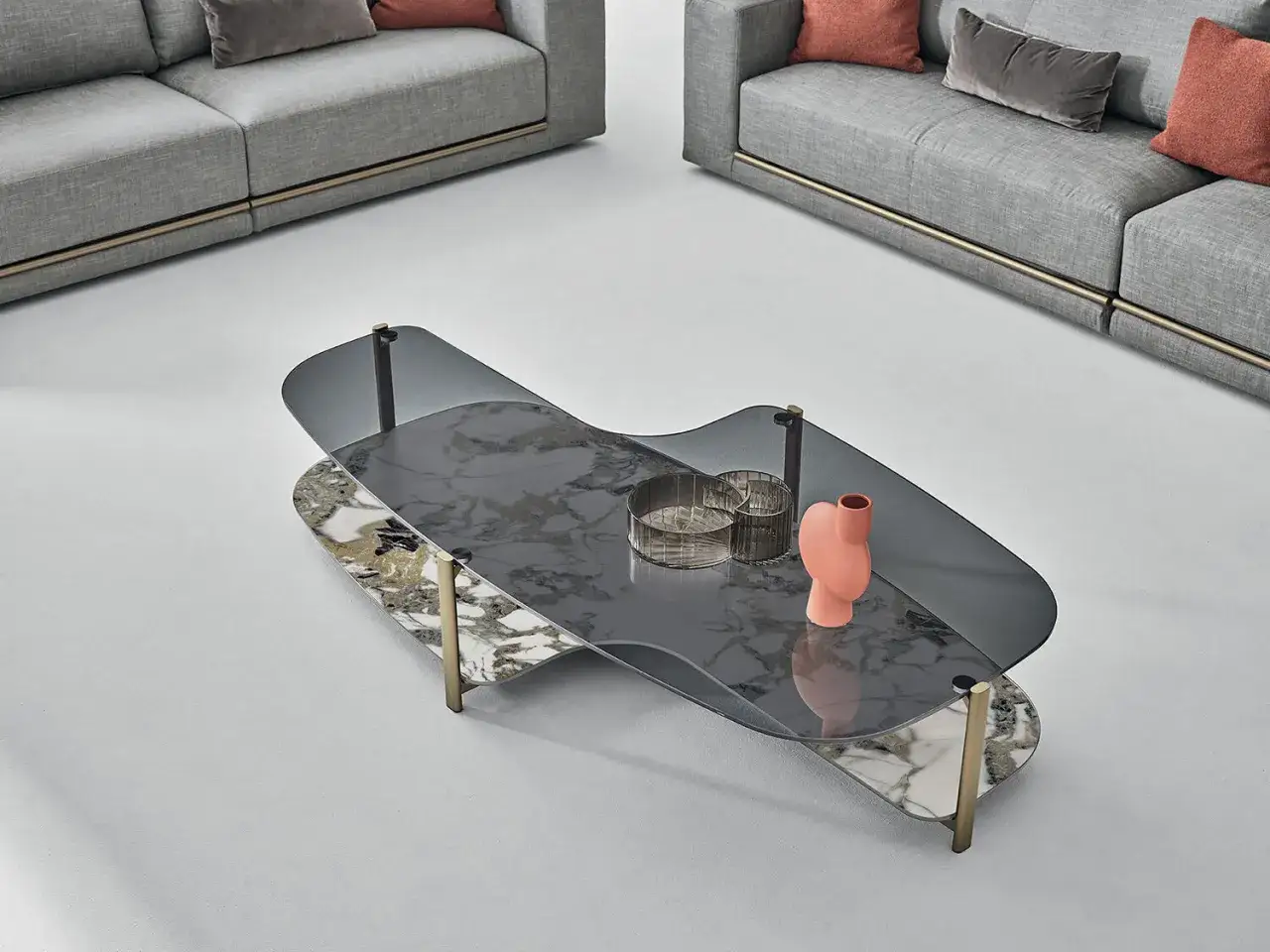 Un tavolino moderno con piano in vetro fum&eacute; e marmo, decorato con un vaso corallo e due portacandele. Perfetto per arredare il tuo salotto.