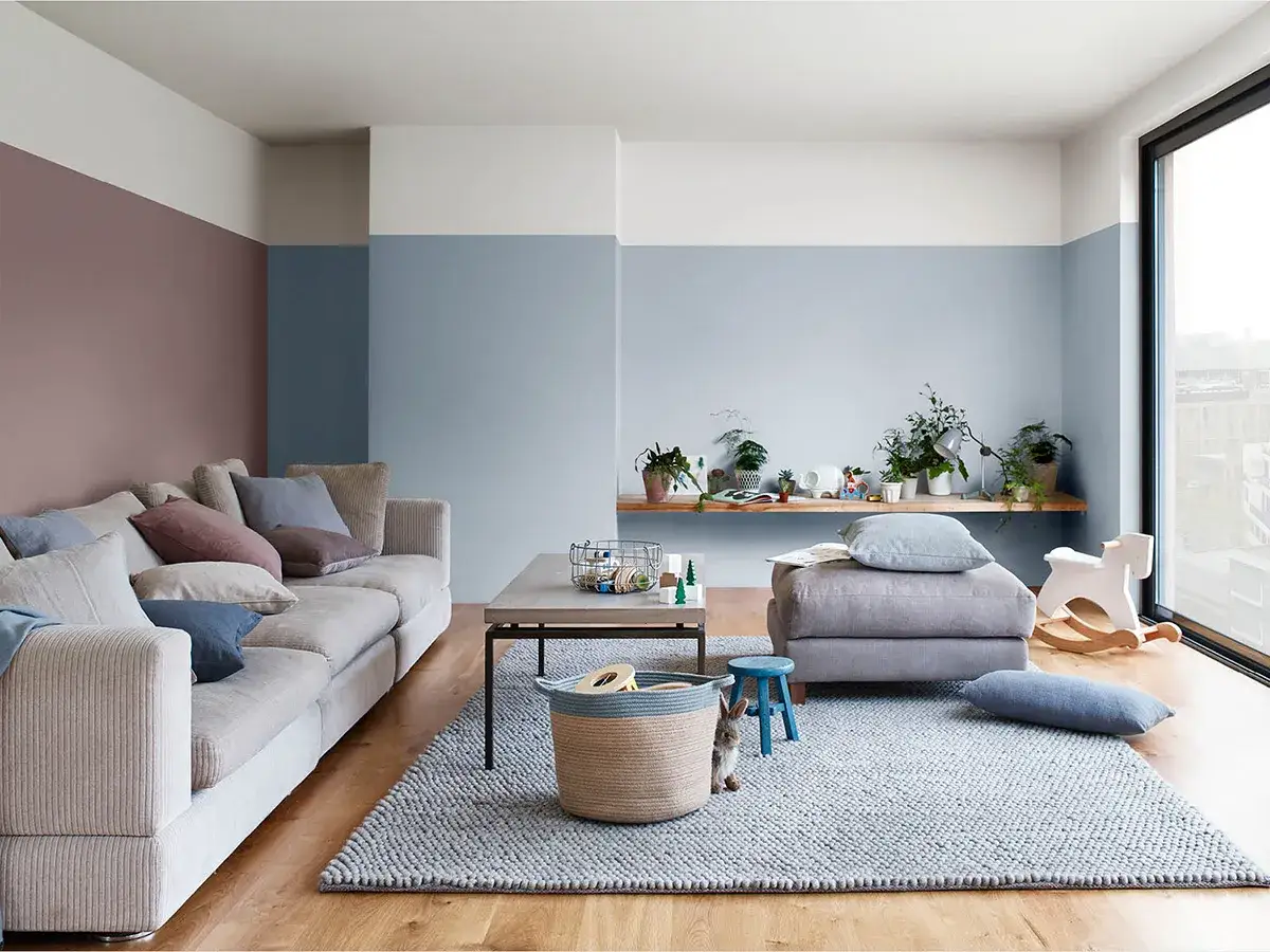 Soggiorno moderno con pareti color carta da zucchero e tortora, divano beige, tappeto grigio e dettagli in legno.