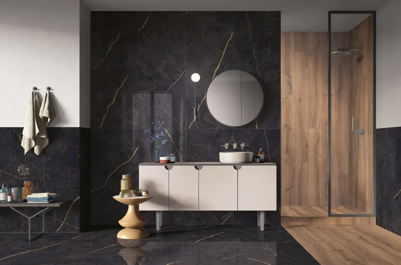 Elegante bagno scuro moderno con finiture in marmo nero e oro, mobile sospeso, specchio rotondo e doccia con rivestimento in legno.