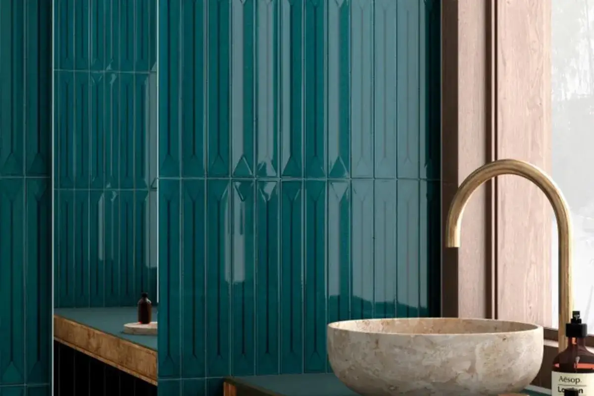 Bagno con piastrelle verde petrolio a rilievo e lavabo in pietra. Dettagli in legno e rubinetto dorato.