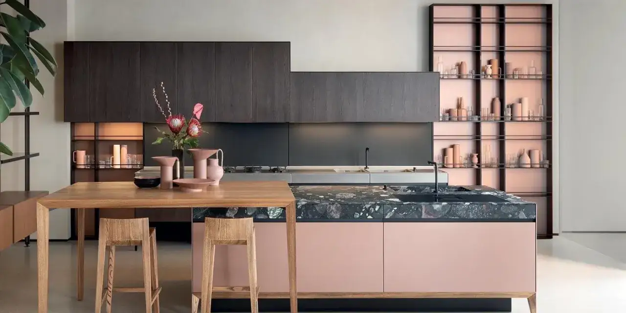 Cucina moderna con isola rosa cipria, piano in pietra scura e pensili in legno scuro. I colori cucina creano un ambiente sofisticato.