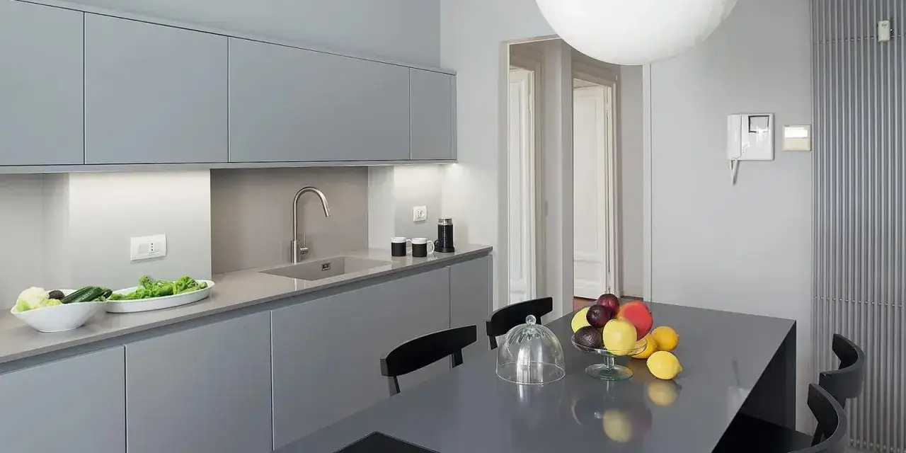 Cucina moderna con mobili grigi e un tavolo con frutta fresca. Il pavimento grigio chiaro completa l'ambiente minimalista.