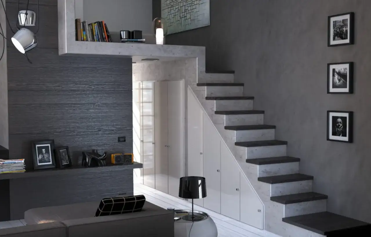 Arredare sottoscala a vista con armadi bianchi integrati. Scale in cemento e legno scuro, quadri in bianco e nero alle pareti.