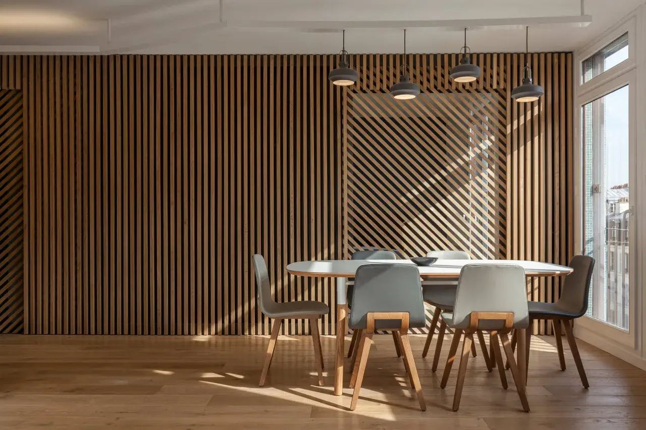 Tavolo da pranzo con sedie grigie davanti a una parete con listelli in legno betulla colore.