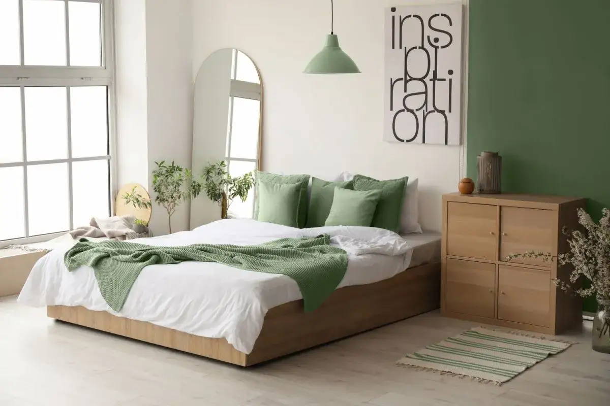 Idee per come rinnovare una vecchia camera da letto: letto con biancheria bianca e plaid verde, specchio ad arco, comodino in legno e piante.