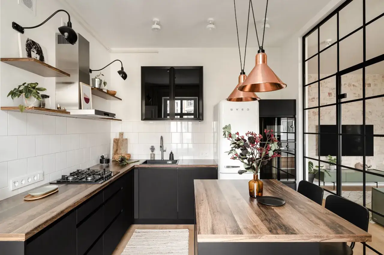 Cucina stile nordico con mobili neri, piano in legno, frigo Smeg bianco e lampade in rame.