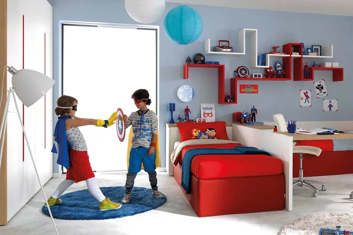 Cameretta con due letti rossi, ideale soluzione cameretta piccola 2 letti. Due bambini vestiti da supereroi giocano.