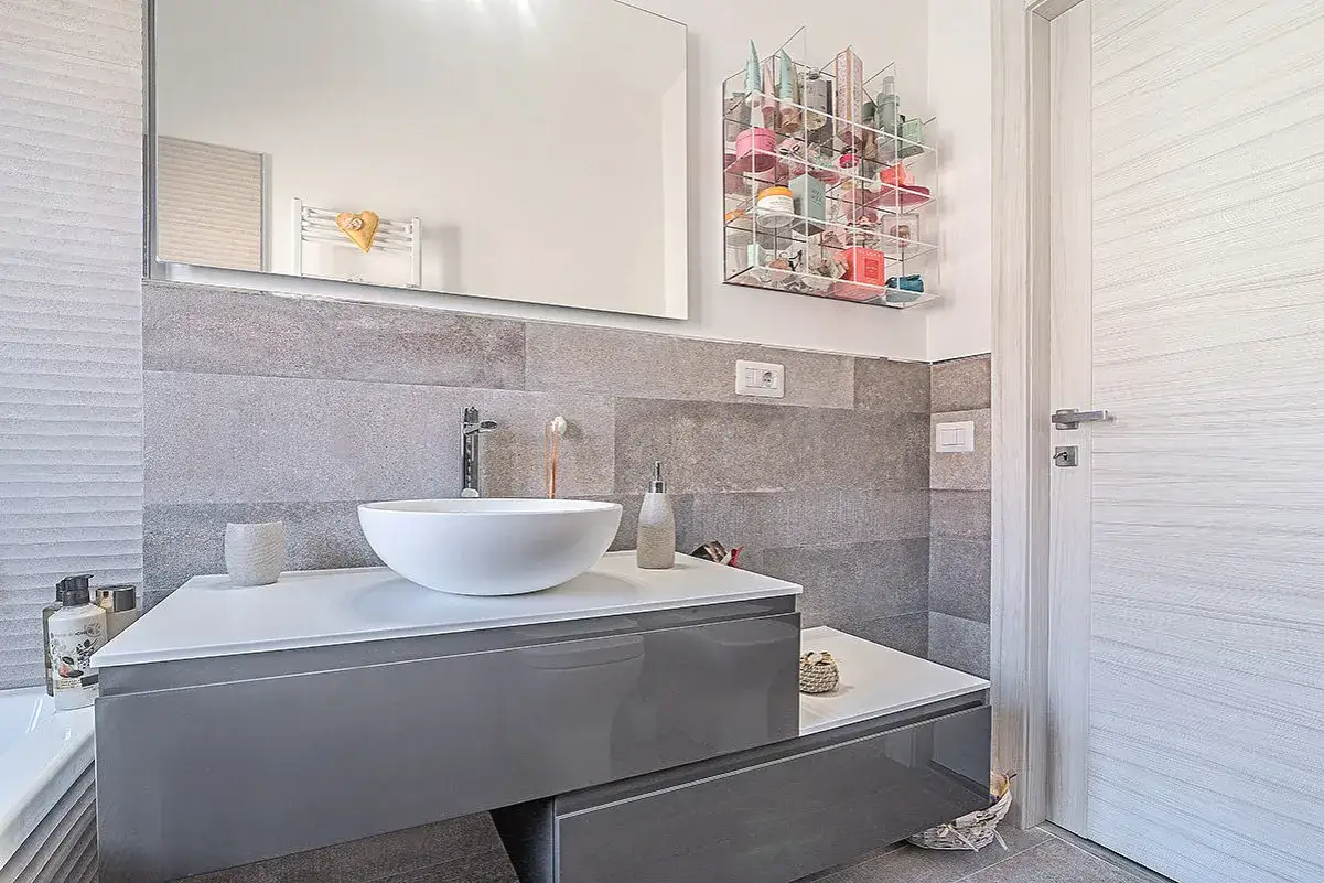Un moderno bagno grigio chiaro e bianco con lavabo a ciotola, mobile sospeso e porta in legno.