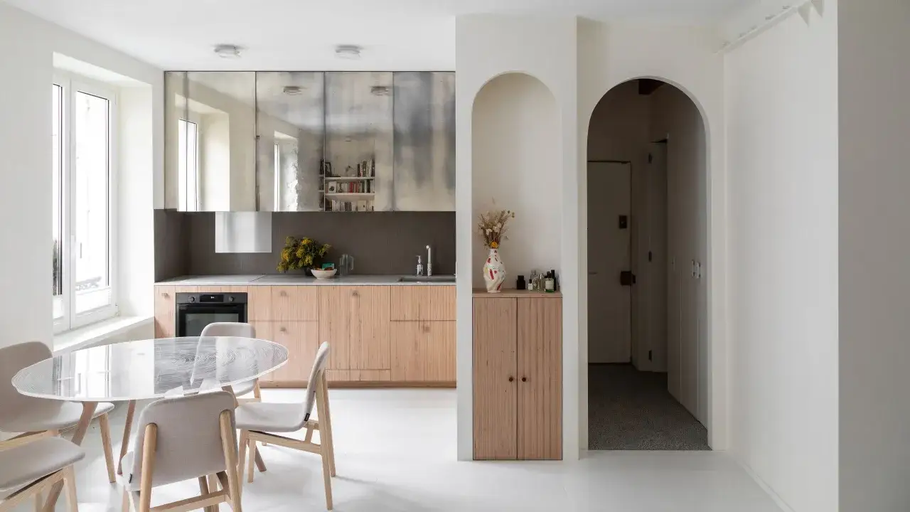 Cucine piccole particolari con mobili in legno chiaro, piano in marmo e pensili a specchio. Tavolo rotondo in vetro e sedie imbottite.