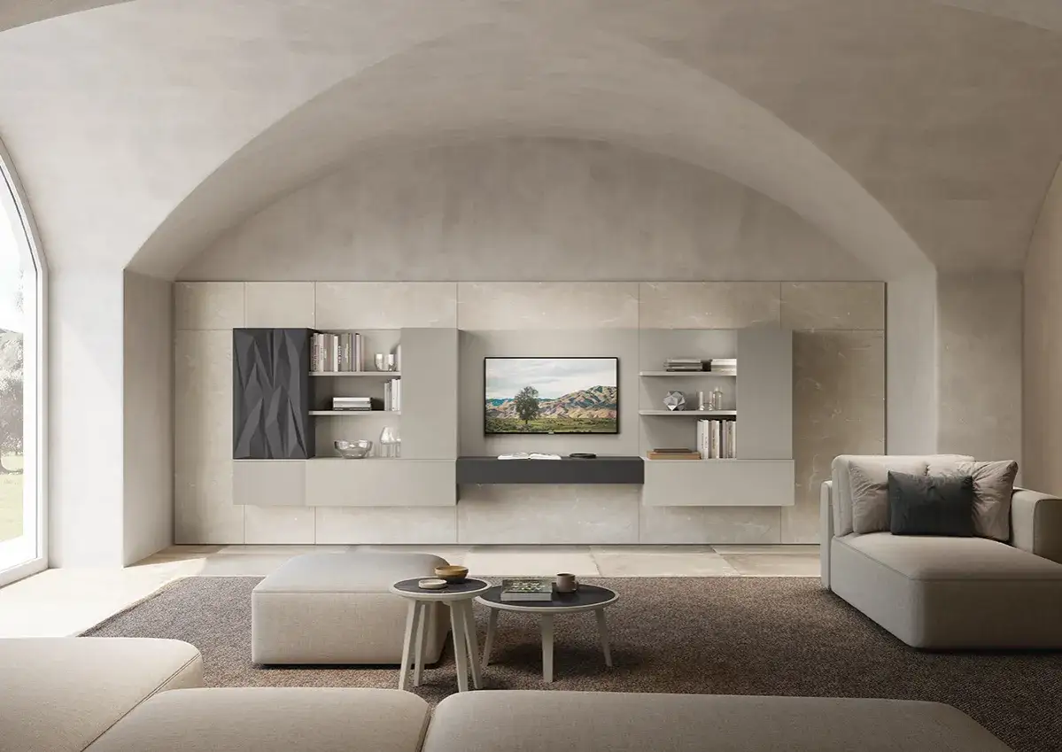 Soggiorno moderno con divano, pouf e tavolini. Le pareti color sabbia dorata incorniciano una parete attrezzata con TV e librerie.