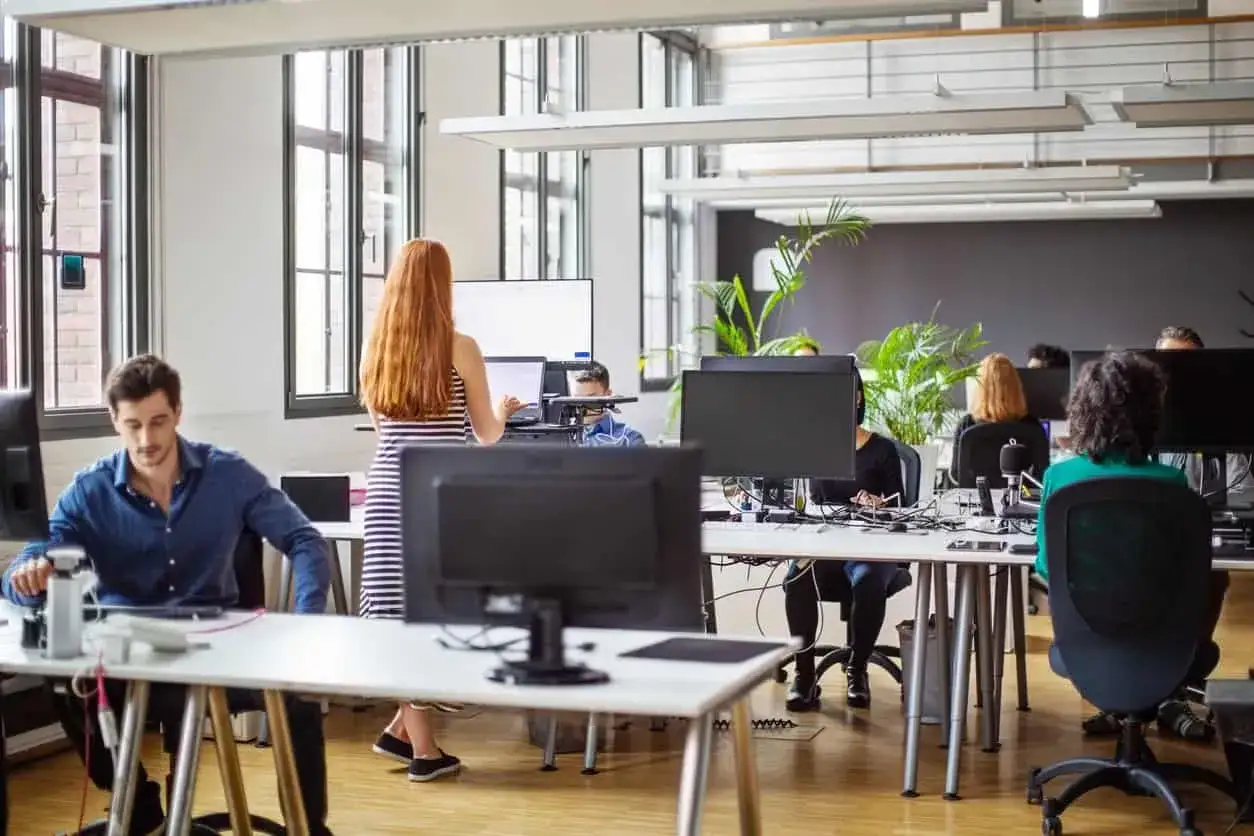 Uomo e donna lavorano in un ufficio moderno. Diverse postazioni con computer e piante verdi creano un ambiente stimolante.