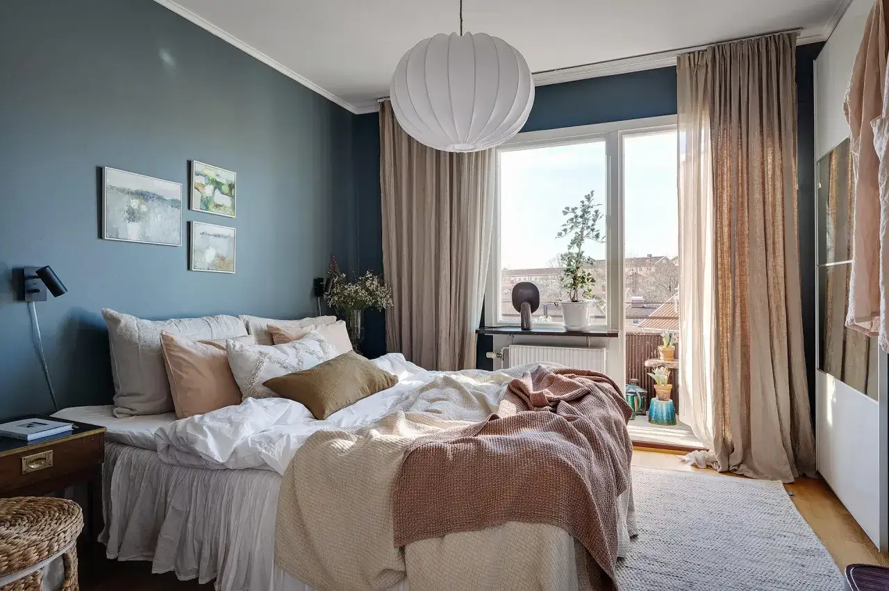 Accogliente camera da letto blu con letto comodo, quadri astratti e una grande finestra che illumina la stanza.