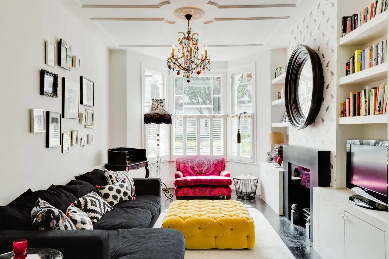 Un salotto con un divano nero, un pouf giallo, una poltrona fucsia e un lampadario colorato. L'arredamento boho glam &egrave; evidente nei dettagli eclettici e nei tessuti vivaci.