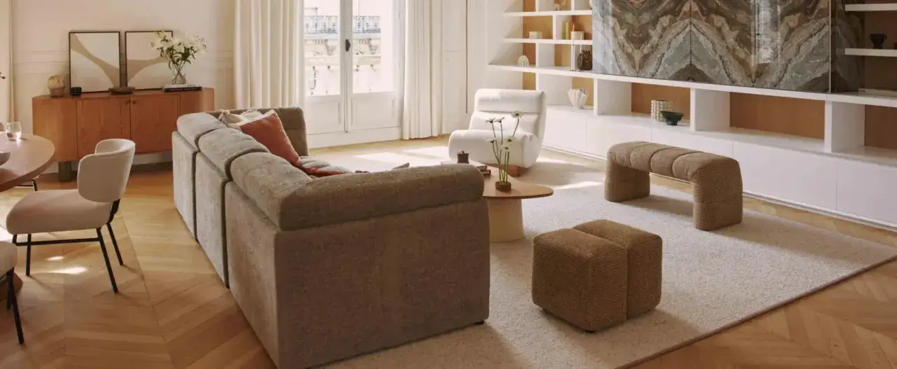 Soggiorno accogliente con divano modulare, poltrona soffice, panca e pouf in tessuto. Parete attrezzata con libreria e un'opera d'arte astratta. Stile contemporaneo casa.