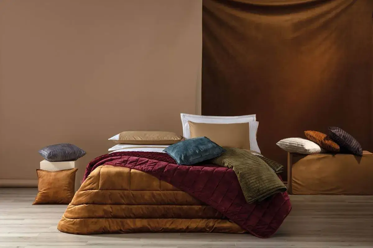 Come mettere il plaid sul letto: un letto accogliente con coperte e cuscini in tonalit&agrave; calde.