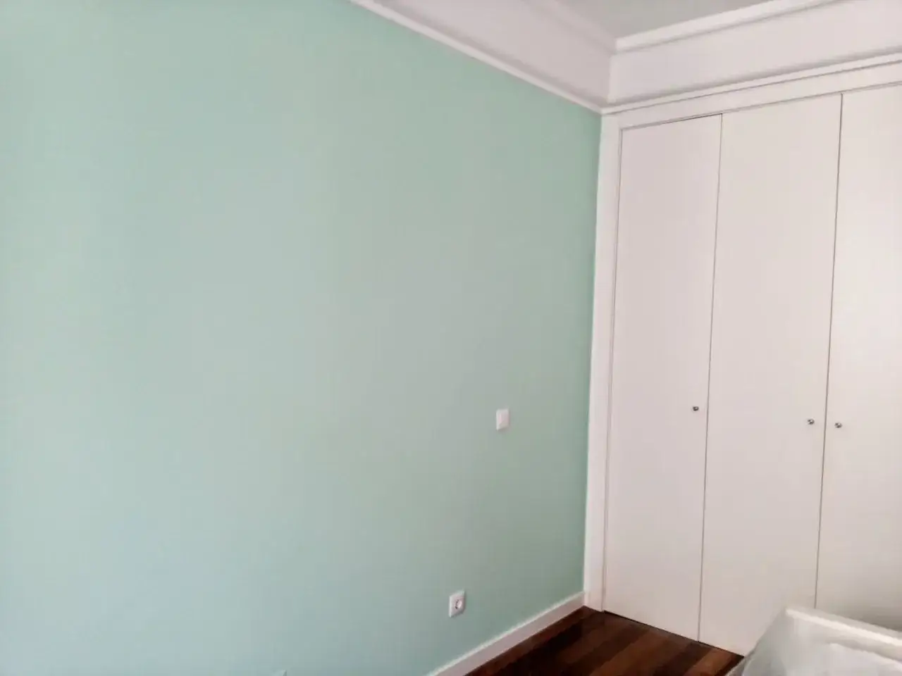 Parete color verde menta, armadio bianco a quattro ante e battiscopa in legno scuro.