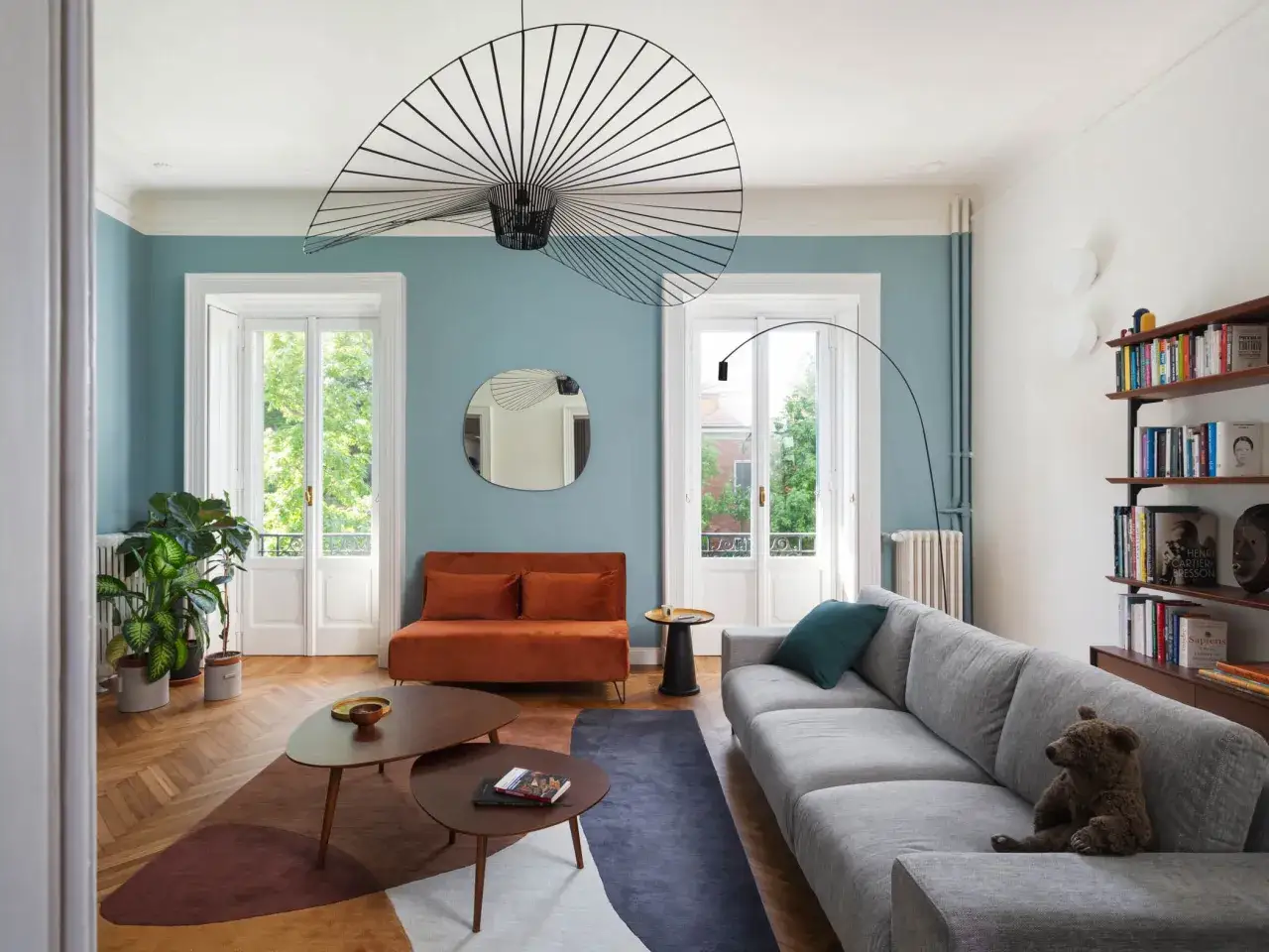 Soggiorno moderno con pareti color tortora e blu polvere, divano grigio, arredi in legno e un tocco di arancio. Idee pareti colorate particolari per un ambiente accogliente.