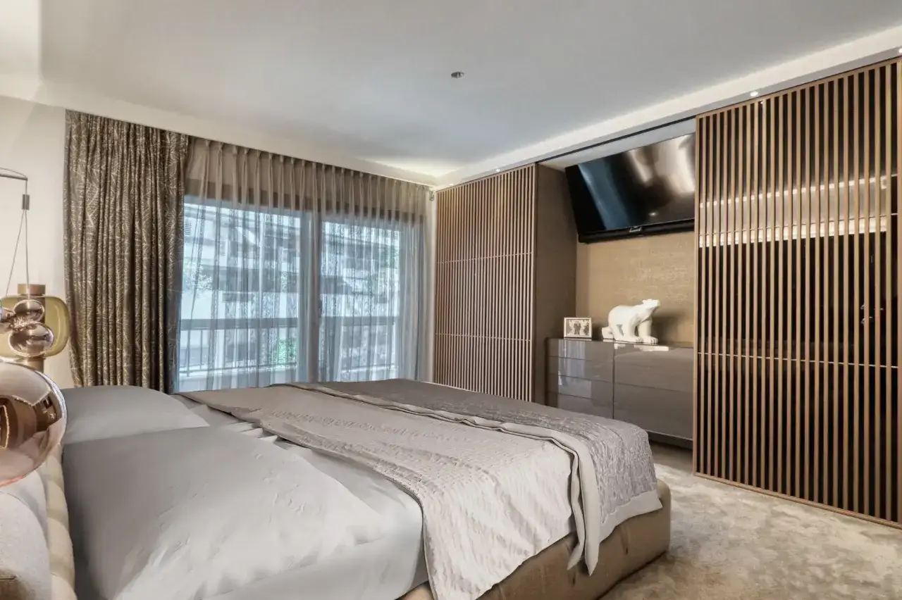 Camera da letto con letto king-size, tende eleganti e un armadio moderno con ante a listelli in legno. I colori neutri e rilassanti creano un'atmosfera serena.