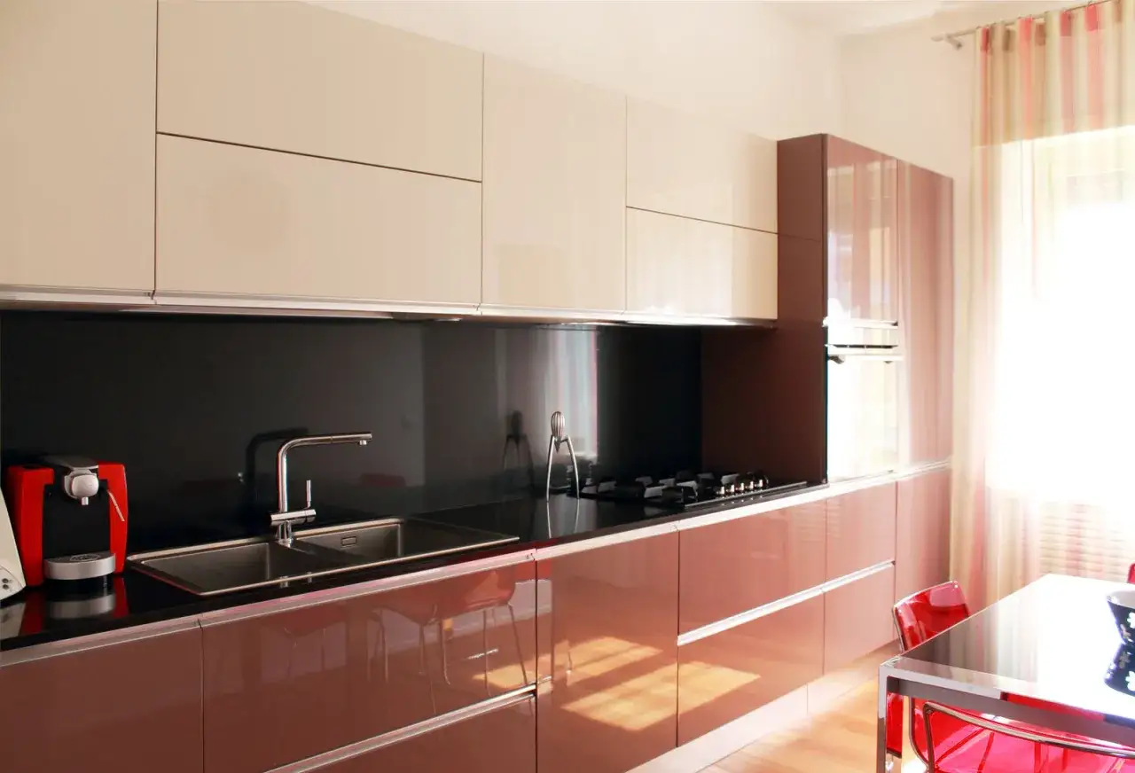 Cucina moderna con pensili chiari e basi color cremisi. Lavello, piano cottura e macchina del caff&egrave; rosse.