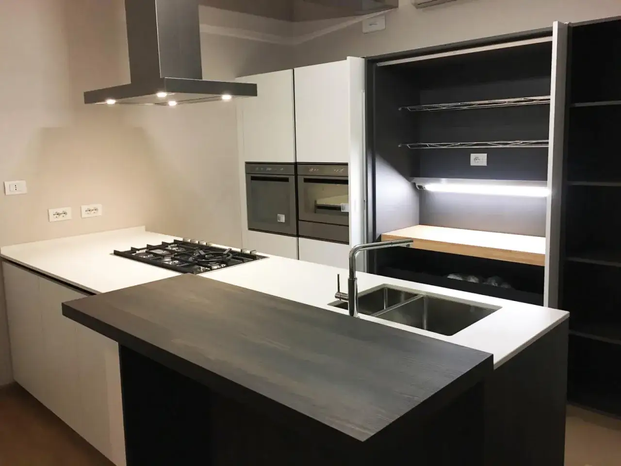 Top cucina con materiali innovativi: piano in quarzo bianco, isola con finitura in legno scuro e un'ampia dispensa a scomparsa.