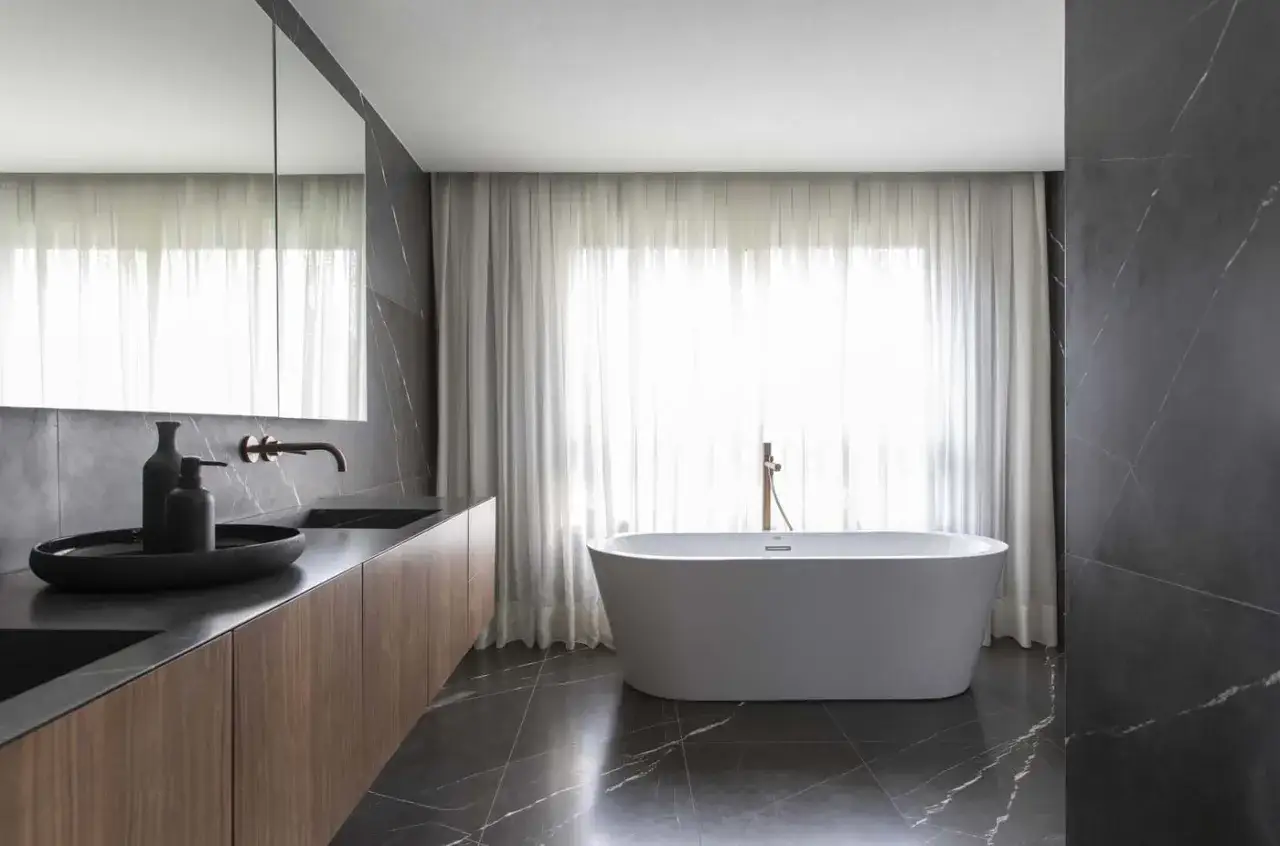 Elegante bagno moderno con vasca freestanding, lavabo in legno e marmo scuro.