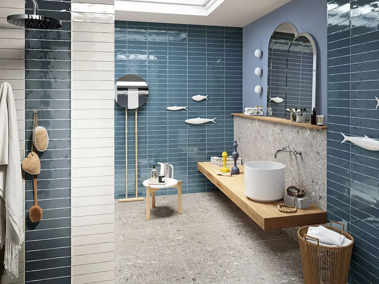 Bagno moderno con piastrelle a righe in tonalit&agrave; bagno azzurro e grigio. Decorazioni a forma di pesce e accessori in legno creano un'atmosfera marina.