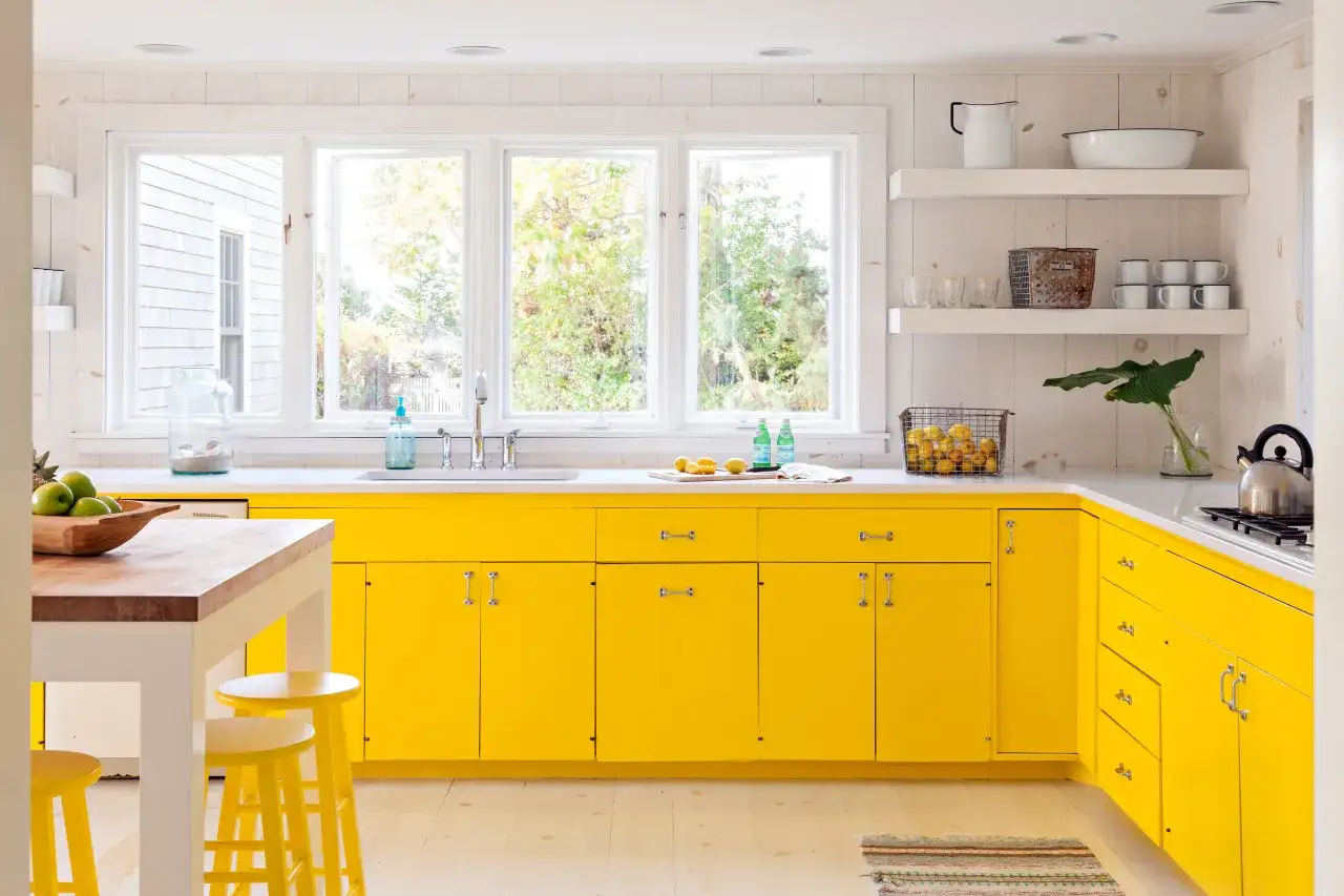 Una luminosa cucina gialla con mobili moderni, un grande lavandino sotto finestre che si affacciano sul verde e un'isola con sgabelli.