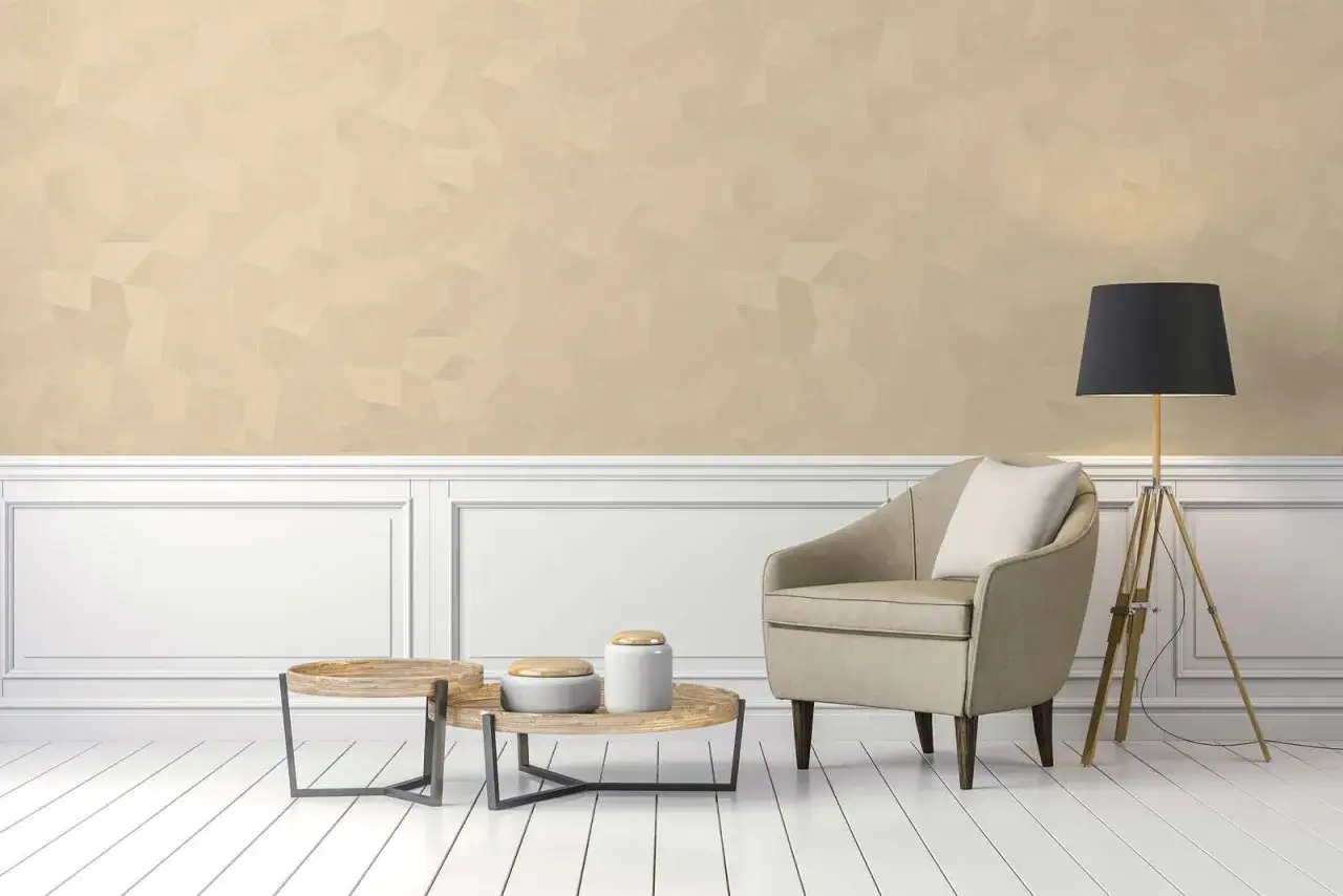 Poltrona beige e tavolini in legno su pavimento bianco, con parete di un caldo color champagne e lampada nera.