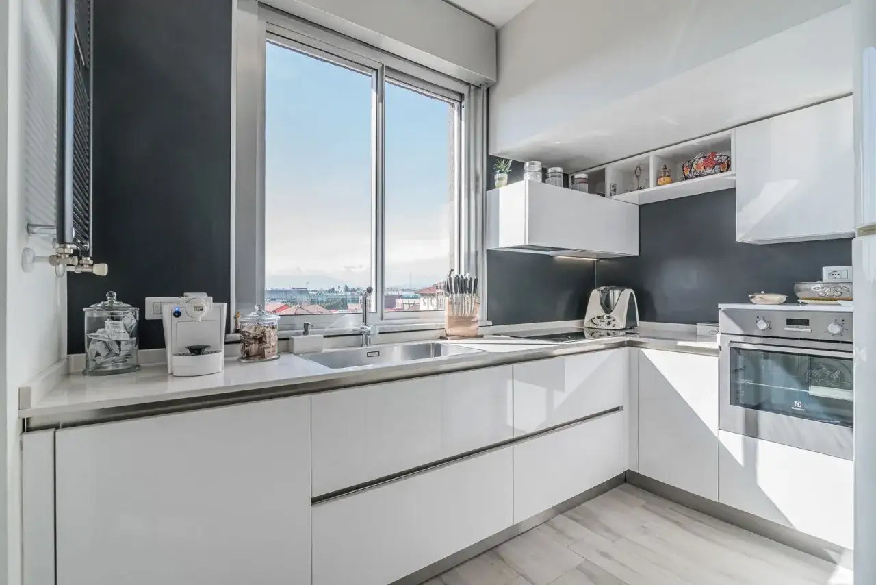 Cucina moderna con ampia finestra che offre una vista panoramica. Elettrodomestici bianchi e finiture lucide creano un ambiente luminoso e funzionale.