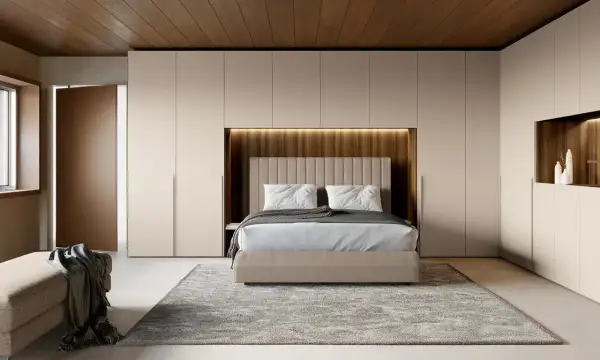 Una moderna zona notte all'ingresso, con letto centrale, armadi a muro e un pouf.