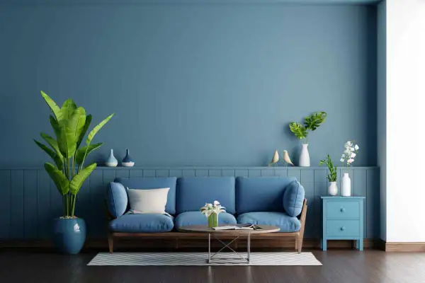 Soggiorno con divano blu e pareti color carta da zucchero. Piante verdi e decorazioni creano un'atmosfera rilassante.