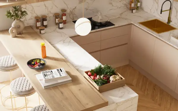 Top cucina con materiali innovativi: piano in legno chiaro, marmo bianco e oro, mobili color pesca. Frutta fresca, verdure e libri sul bancone.