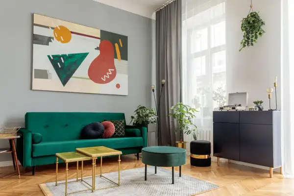 Soggiorno moderno con divano verde smeraldo, tavolini dorati e un quadro astratto. Un esempio di come abbinare i colori con stile.