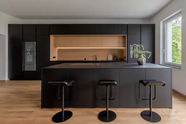 Moderna cucina nera con isola centrale e sgabelli. Un'elegante nicchia in legno chiaro illumina lo spazio, offrendo splendide idee cucina nera e legno.